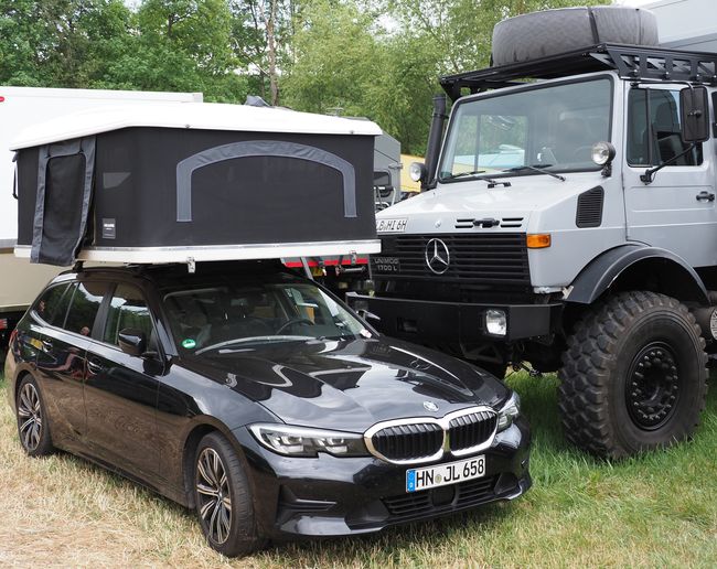 Sportieve BMW personenauto met overmaatse daktent en een Unimog U 1700 L